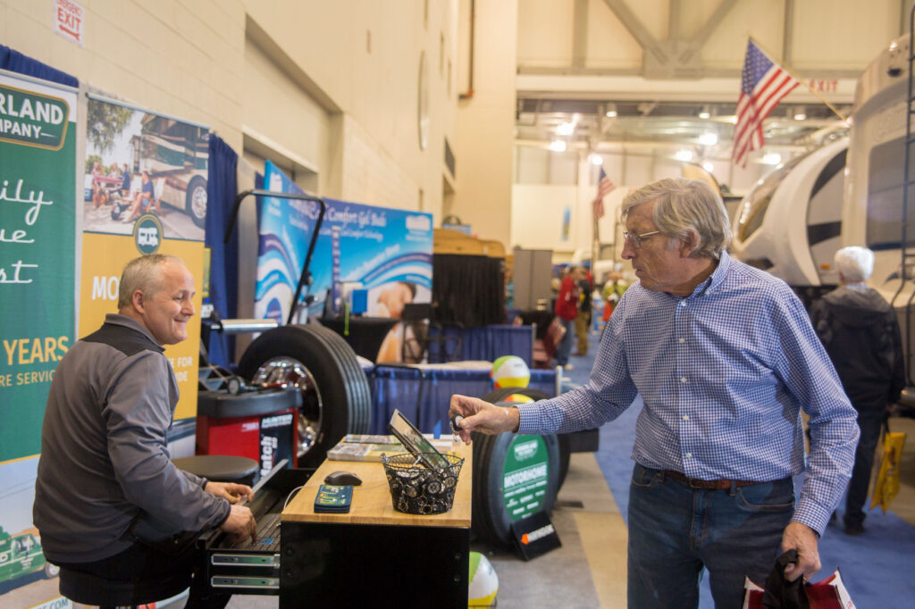 A man taking a Wonderland Tire keychain from a basket at a trade show 