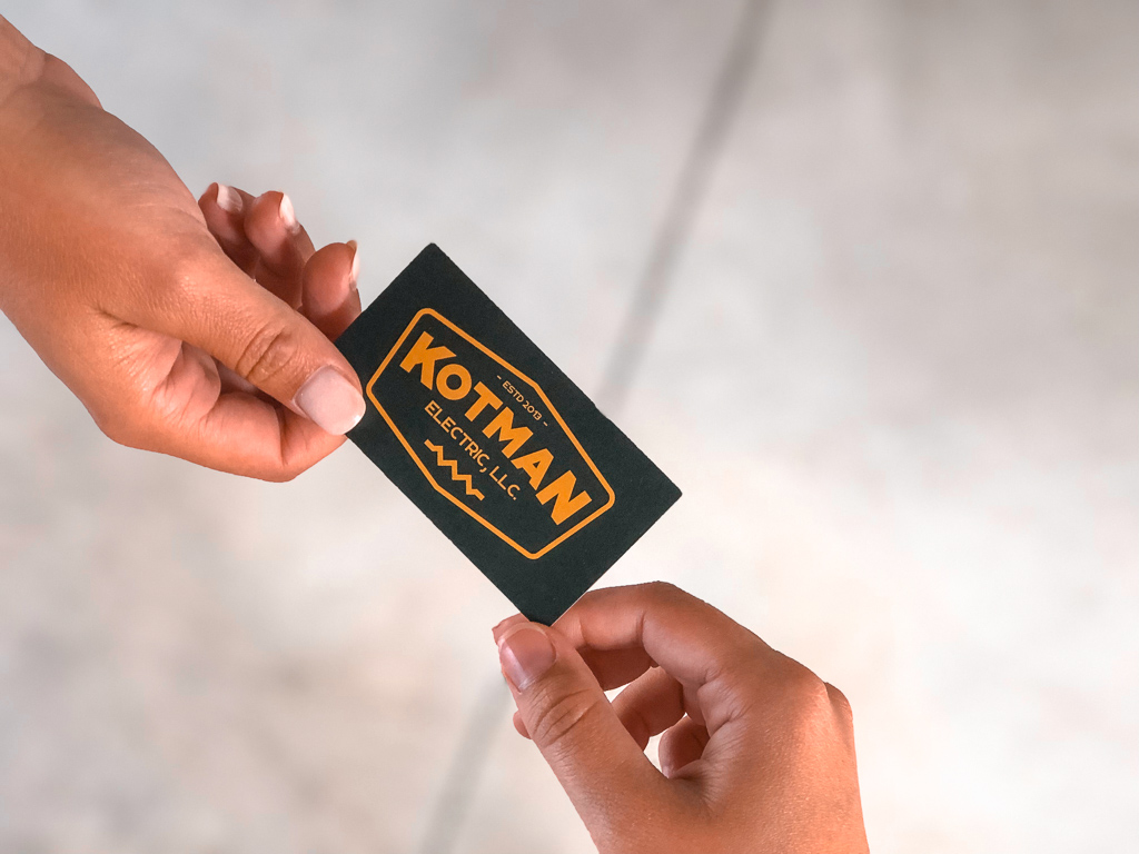 Someone handing a Kotman Electric business card to someone else