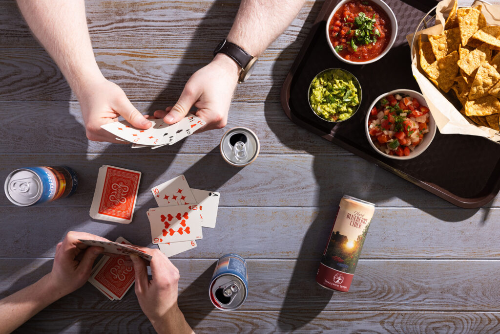 Two people playing cards while enjoying Tanglewood Winery canned wines